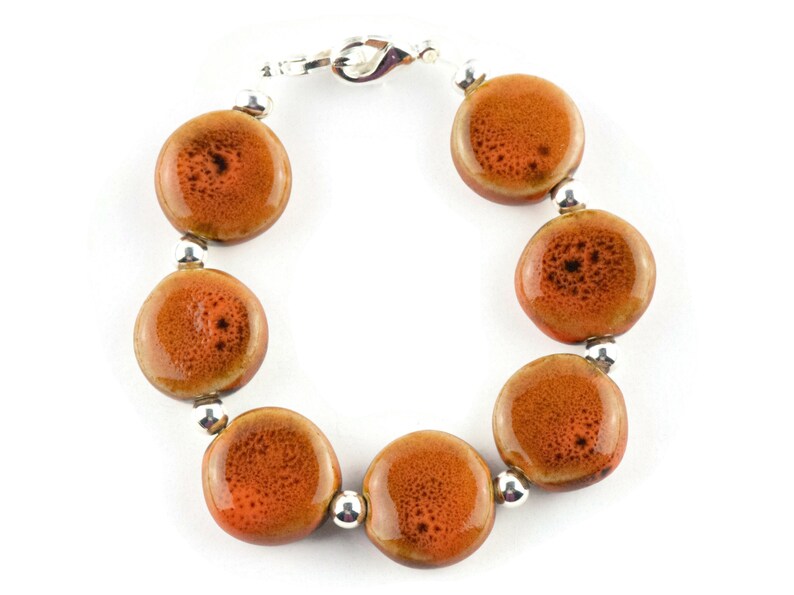 May include: A bracelet made with round, orange ceramic beads and silver spacers. The bracelet has a silver clasp.