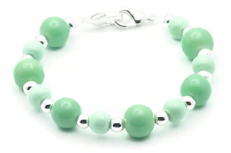 May include: A green and silver beaded bracelet with a silver clasp. The bracelet is made with round beads of varying sizes.