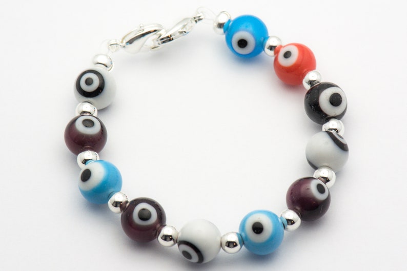 Puede incluir: Un brazalete con cuentas de plata y cuentas de vidrio de colores con dise&ntilde;os de ojo turco. Las cuentas son azules, rojas, negras y blancas.