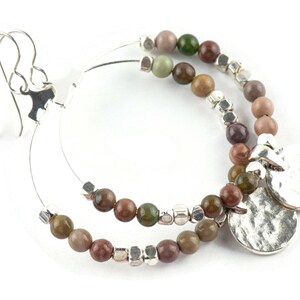 May include: Silver hoop earrings with a double row of brown, green, and gray gemstone beads and two silver charm pendants.
