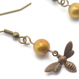May include: Gold tone earrings with a single golden pearl and a small bee charm hanging from each earring.