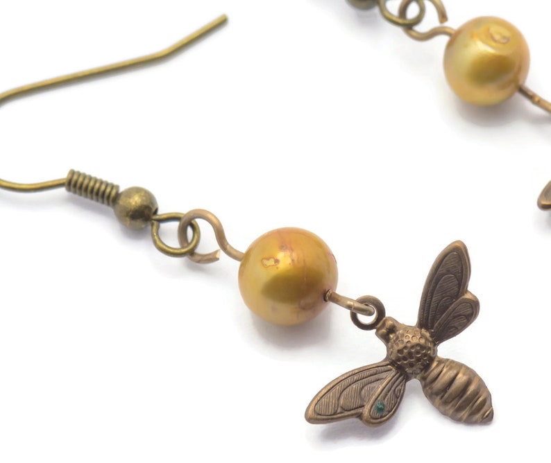 May include: Gold tone earrings with a single golden pearl and a small bee charm hanging from each earring.