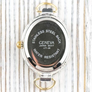 May include: Close-up of the back of a Geneva watch. The watch has a stainless steel back and is water resistant. The text on the watch reads "GENEVA JAPAN MOVT LTT-20". The watch has gold-colored accents.