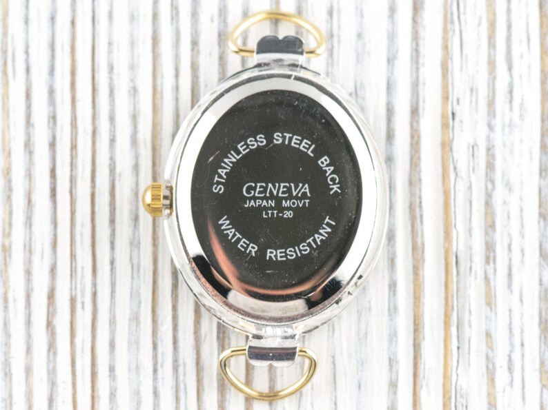 May include: Close-up of the back of a Geneva watch. The watch has a stainless steel back and is water resistant. The text on the watch reads "GENEVA JAPAN MOVT LTT-20". The watch has gold-colored accents.