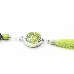 May include: A green and white ceramic bead with a floral design, a brown bead with a green floral design, and a green tassel on a silver chain.