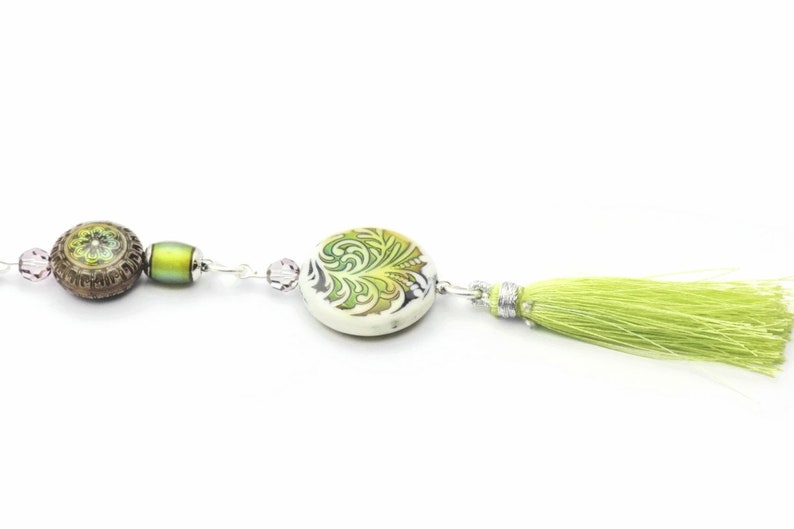 May include: A green and white ceramic bead with a floral design, a brown bead with a green floral design, and a green tassel on a silver chain.