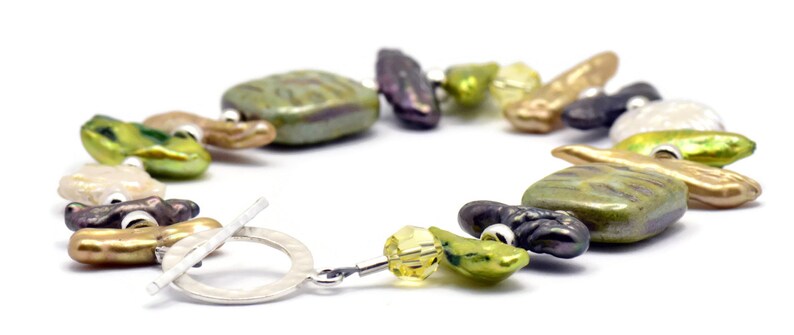K&ouml;nnte beinhalten: Ein Armband aus S&uuml;&szlig;wasserperlen in Gr&uuml;n, Braun und Gold mit einem silbernen Schiebeverschluss. Das Armband verf&uuml;gt &uuml;ber eine Vielzahl von Formen und Gr&ouml;&szlig;en von Perlen, darunter runde, ovale und quadratische.