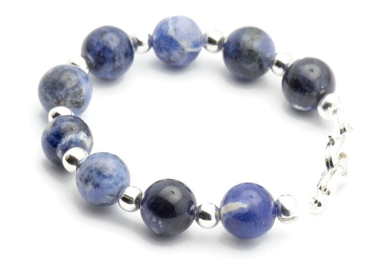 K&ouml;nnte beinhalten: Ein Armband aus blauen und wei&szlig;en Edelsteinen mit silbernen Perlen und einem silbernen Verschluss.