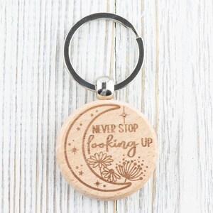 May include: Wooden keychain with a crescent moon design and the text "Never Stop Looking Up". The keychain has a silver key ring.