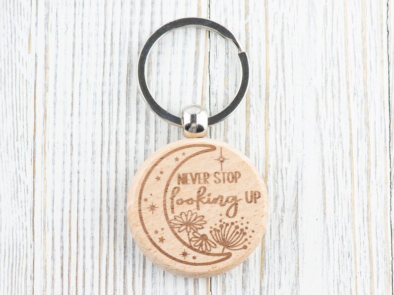 May include: Wooden keychain with a crescent moon design and the text "Never Stop Looking Up". The keychain has a silver key ring.