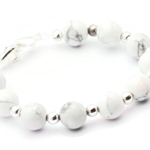 May include: A bracelet featuring white and grey marbled stone beads, interspersed with small silver-coloured beads. The bracelet has a silver clasp and is designed to be worn around the wrist.