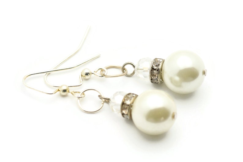 Peut inclure: Une paire de boucles d'oreilles pendantes en argent avec des accents de perles blanches et de cristal.