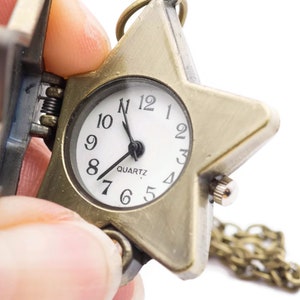 Peut inclure: Une montre de poche en forme d'&eacute;toile dor&eacute;e avec un cadran blanc et des aiguilles noires. La montre est &agrave; quartz et est attach&eacute;e &agrave; une cha&icirc;ne dor&eacute;e.
