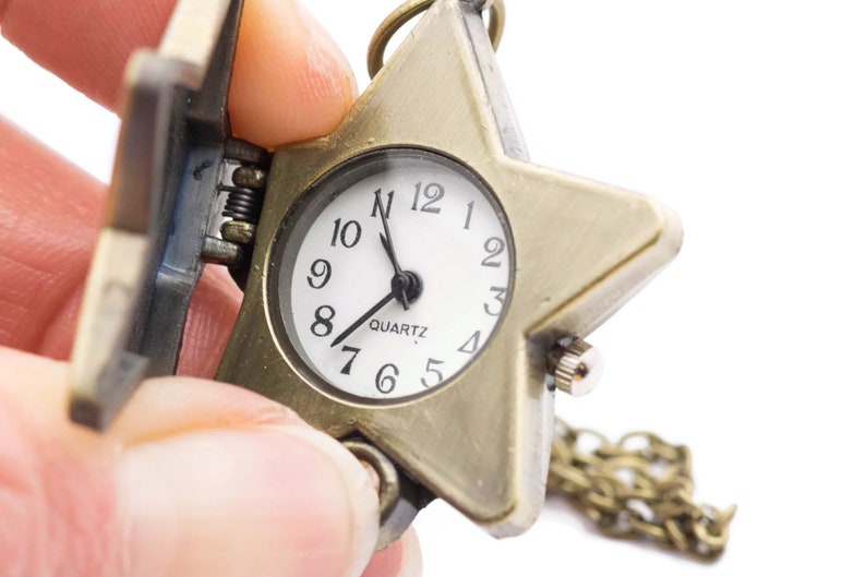 Peut inclure: Une montre de poche en forme d'&eacute;toile dor&eacute;e avec un cadran blanc et des aiguilles noires. La montre est &agrave; quartz et est attach&eacute;e &agrave; une cha&icirc;ne dor&eacute;e.