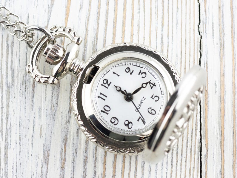 May include: A silver pocket watch with a white face and black hands. The watch has a chain attached to it and is open to reveal the inner workings.