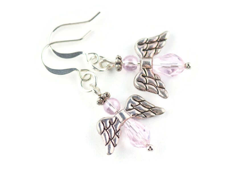 May include: A pair of silver angel wing earrings with pink crystal beads. The earrings have a hook closure.