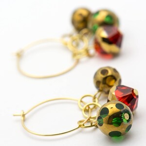 Puede incluir: Aretes de aro de oro con colgantes. Los colgantes son una mezcla de cuentas de vidrio doradas, rojas y verdes.
