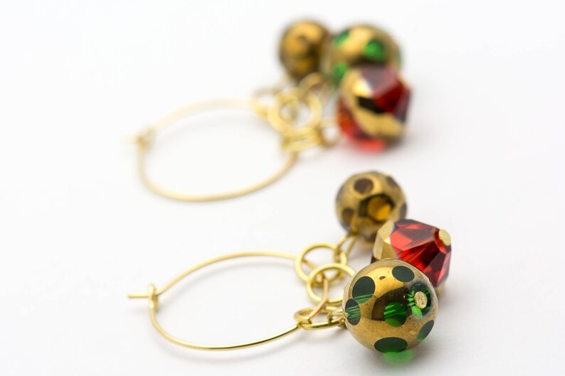 Puede incluir: Aretes de aro de oro con colgantes. Los colgantes son una mezcla de cuentas de vidrio doradas, rojas y verdes.