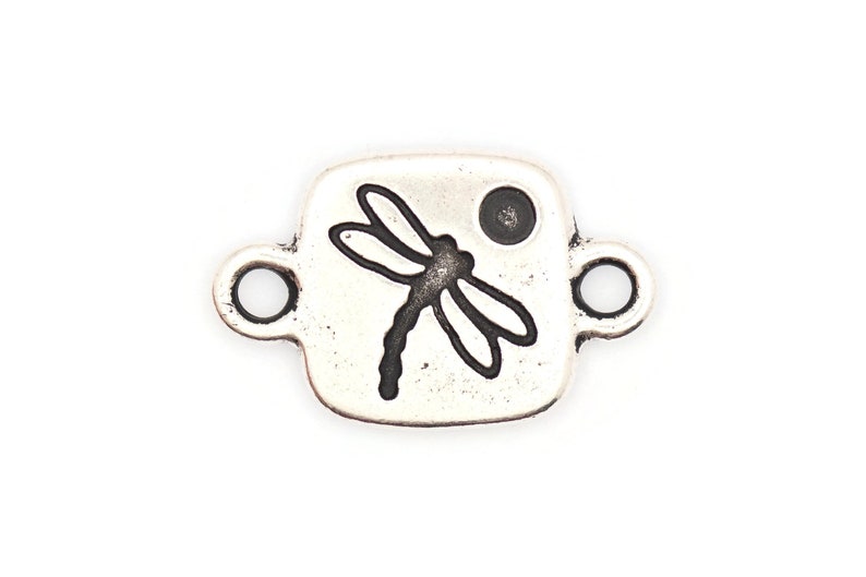 May include: Silver-toned metal charm with a dragonfly design and a small circle. The charm has two loops for attaching to a bracelet or necklace.