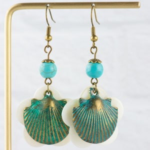 May include: A pair of dangle earrings featuring a turquoise bead, a white shell, and a green and gold seashell charm.