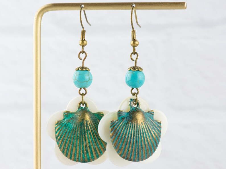 May include: A pair of dangle earrings featuring a turquoise bead, a white shell, and a green and gold seashell charm.