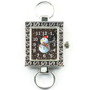 K&ouml;nnte beinhalten: Silberner Schl&uuml;sselanh&auml;nger mit Uhr, schwarzes Zifferblatt mit Schneemann-Motiv und dem Text "GENEVA".