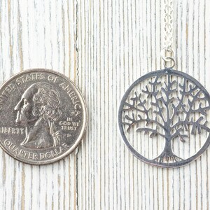 K&ouml;nnte beinhalten: Eine silberne Halskette mit einem Lebensbaum-Anh&auml;nger. Der Anh&auml;nger ist ein Kreis mit einem detaillierten Baumdesign, das aus dem Metall ausgeschnitten ist. Die Halskette wird neben einem US-amerikanischen Vierteldollar zur Gr&ouml;&szlig;envergleich gezeigt.
