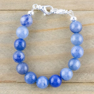 May include: A blue gemstone bracelet with a silver clasp. The bracelet is made of round beads that are graduated in size, with the largest beads in the centre. The beads are a light blue colour, with a hint of white.