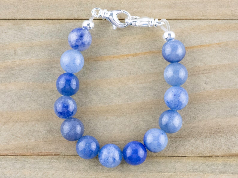 May include: A blue gemstone bracelet with a silver clasp. The bracelet is made of round beads that are graduated in size, with the largest beads in the centre. The beads are a light blue colour, with a hint of white.
