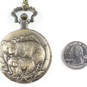 May include: A bronze pocket watch with a detailed design of a mother bear and her cub. The watch is about the size of a US quarter.
