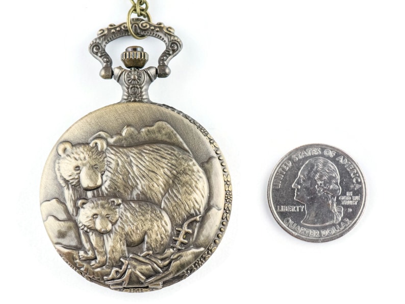 May include: A bronze pocket watch with a detailed design of a mother bear and her cub. The watch is about the size of a US quarter.