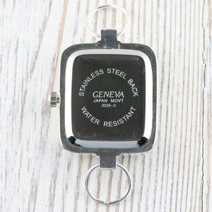 Pu&ograve; includere: Il retro di un orologio quadrato argentato con la scritta "Stainless Steel Back Geneva Japan Movt 2039-S Water Resistant" stampata su di esso.