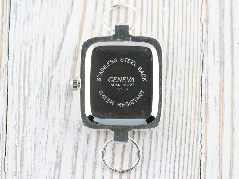Pu&ograve; includere: Il retro di un orologio quadrato argentato con la scritta "Stainless Steel Back Geneva Japan Movt 2039-S Water Resistant" stampata su di esso.