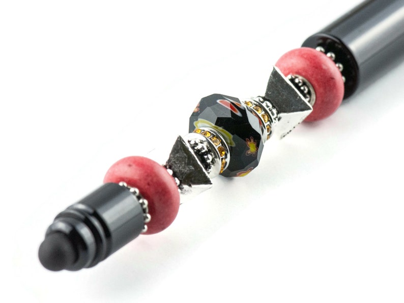 May include: A black stylus pen with a decorative design featuring red, black and silver beads. The beads are arranged in a pattern and have a sparkly finish.