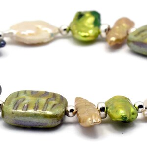 K&ouml;nnte beinhalten: Ein Armband aus gr&uuml;nen, braunen und wei&szlig;en Barockperlen mit silbernen Akzenten. Die Perlen sind unregelm&auml;&szlig;ig geformt und haben ein nat&uuml;rliches, organisches Aussehen.