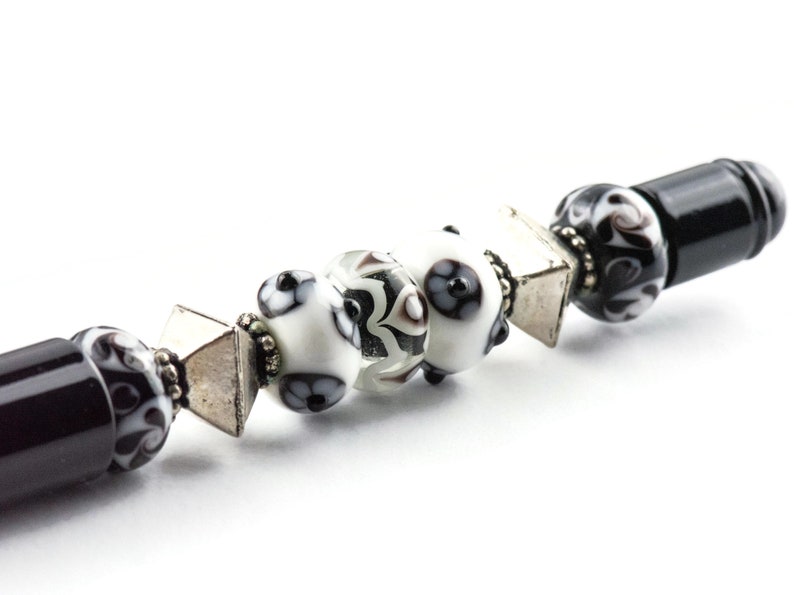 May include: A black pen with a silver and black patterned design. The pen has a black and white patterned cap with silver accents.