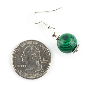 May include: Green malachite gemstone dangle earrings with silver hooks. The earrings are shown next to a US quarter for size reference.