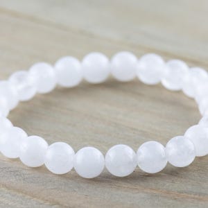 May include: A white gemstone bracelet with round beads. The bracelet is made of natural stones and is designed to be worn on the wrist.