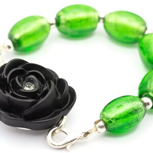 May include: A black rose charm bracelet with green glass beads. The rose has a small rhinestone in the center.