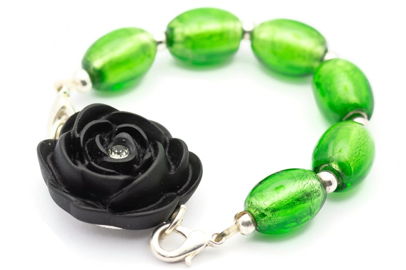 May include: A black rose charm bracelet with green glass beads. The rose has a small rhinestone in the center.