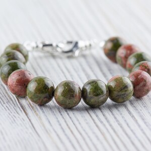 Puede incluir: Un brazalete de piedras preciosas verdes y rojas con un cierre de plata. El brazalete est&aacute; hecho de cuentas redondas y tiene una longitud aproximada de 18 cm.