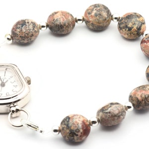May include: A silver watch with a square face and a brown and white speckled stone bracelet.
