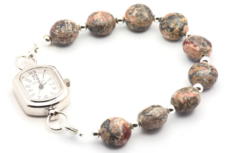 May include: A silver watch with a square face and a brown and white speckled stone bracelet.