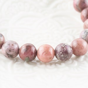 May include: A pink and white gemstone bracelet with round beads. The beads have a mottled pattern.