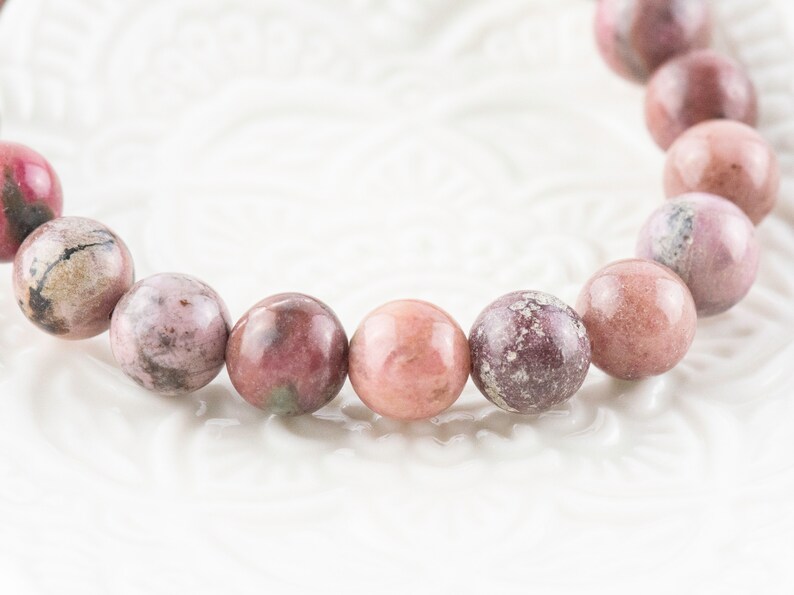 May include: A pink and white gemstone bracelet with round beads. The beads have a mottled pattern.