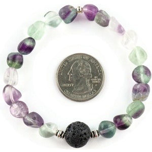 Puede incluir: Un brazalete hecho con cuentas de fluorita verde, p&uacute;rpura y transparente, y una cuenta de lava negra. El brazalete es aproximadamente del tama&ntilde;o de una moneda de 25 centavos de d&oacute;lar estadounidense.