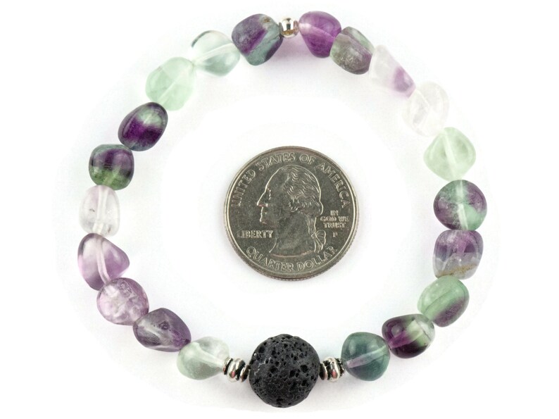 Puede incluir: Un brazalete hecho con cuentas de fluorita verde, p&uacute;rpura y transparente, y una cuenta de lava negra. El brazalete es aproximadamente del tama&ntilde;o de una moneda de 25 centavos de d&oacute;lar estadounidense.