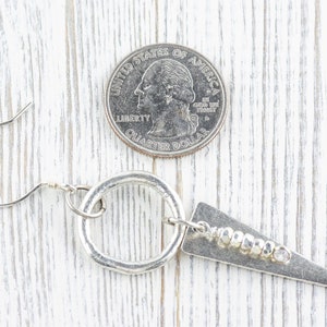 May include: Silver earrings with a hammered circle and a triangle pendant with a row of silver beads. The earrings are shown next to a US quarter for size reference.