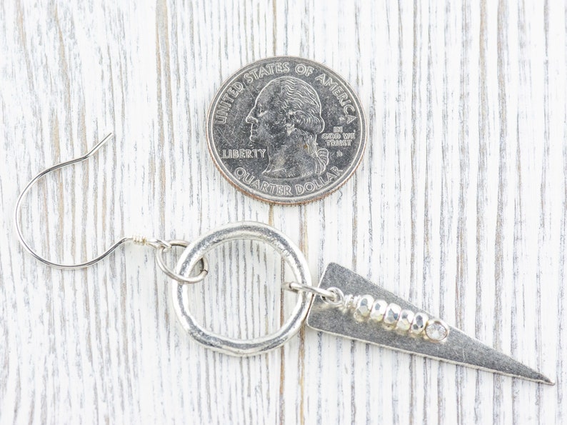 May include: Silver earrings with a hammered circle and a triangle pendant with a row of silver beads. The earrings are shown next to a US quarter for size reference.