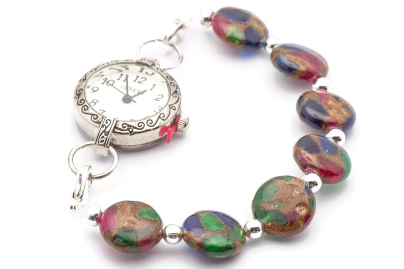 May include: A silver pocket watch with a white face and black hands attached to a bracelet made of colorful glass beads. The beads are oval shaped and have a gold, green, blue, and red speckled pattern.